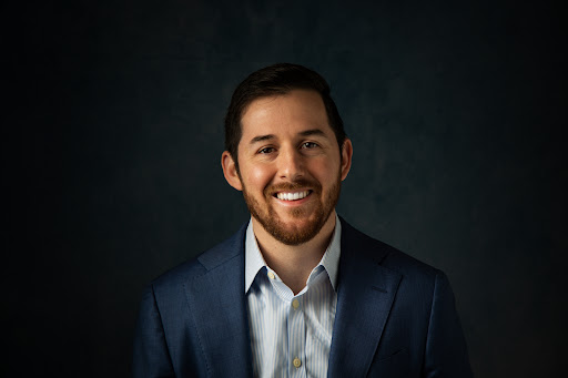 Headshot example photo of a smiling man in a blue blazer against a dark studio background